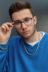 Stylish portrait of a fashion handsome young guy with a beard and haircut in a trendy blue...