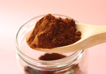 Ground coffee powder and spoon close up view, with glass jar on pink background