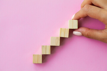 Hand arranging wood cube stacking as step stair.