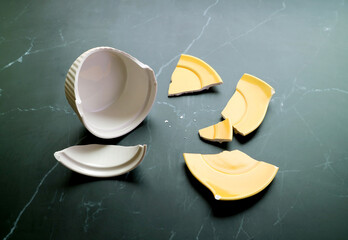 Broken white and yellow pottery scattered on black kitchen floor