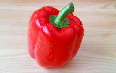Closeup of a red bell pepper with water droplets isolated on wooden backdrop