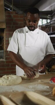 Vertical video of african american male baker preparing dough in bakery