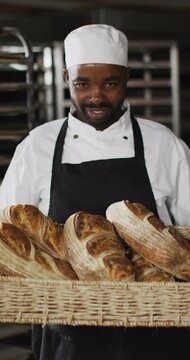 Vertical video of portrait of happy african american male baker with bread in bakery