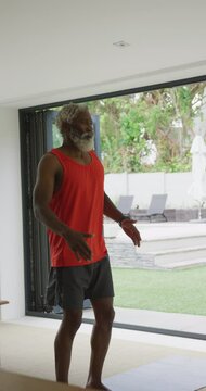 Vertical video of senior african american man practicing yoga at home