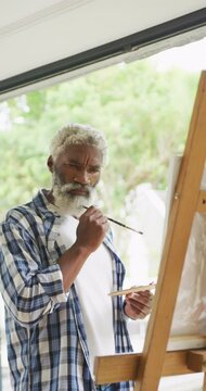 Vertical video of senior african american man painting at home