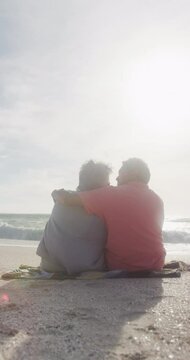 Vertical video of happy senior biracial couple embracing on sunny beach