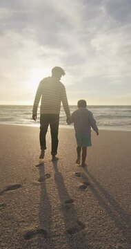 Vertical video of biracial father with son walking on sunny beach