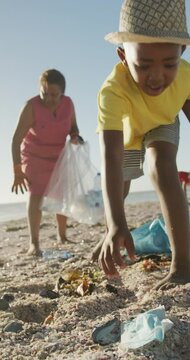 Vertical video of happy african american family segregating waste on sunny beach