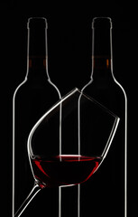 Glass and bottles of red wine on a black background.