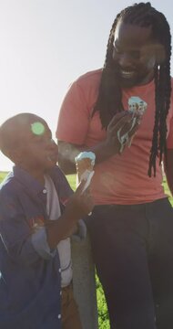 Vertical video of happy african american father with son with ice cream