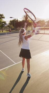 Vertical video of caucasian female tennis player with ball and tennis racket