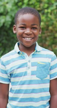 Vertical video of portrait of happy african american boy in garden