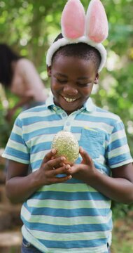 Vertical video of portrait of happy african american boy with egg at easter
