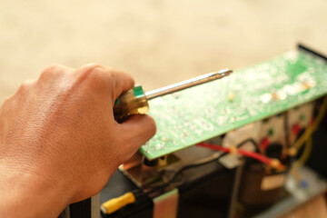 Closeup of a man holding a screwdriver troubleshooting and repairing a UPS machine. Electronics technician