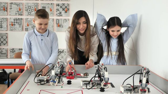 Young beautiful mother with her son and daughter play in the school of robotics with robots from the constructor.