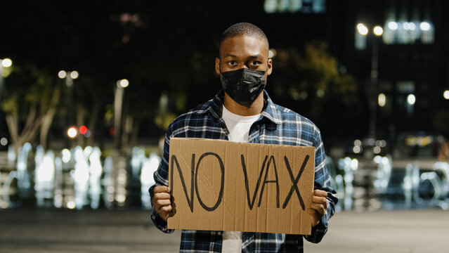 Portrait Angry African American Man In Face Mask Stands In City At Night Evening Holding Sign Banner With Text No VAX Guy Protest Of Covid 19 Vaccine Stop Immunization Concept. Vaccination Phobia