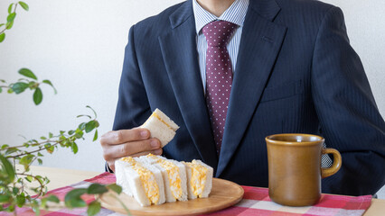 玉子サラダサンドイッチを食べるビジネスマン｜朝食・昼食・間食イメージ。