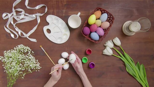 Top view of a table with items to create a composition for Easter. Women's hands paint Easter eggs with colored paint. Church holiday-Easter