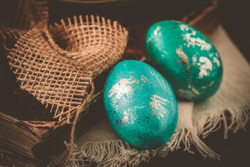 Two green and turquoise easter eggs with metallic effect on dark brown vintage background