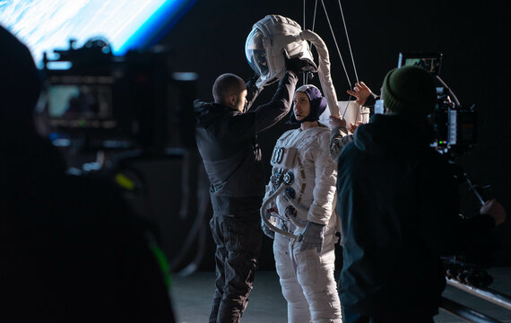 Behind the scenes - Caucasian female stuntwoman wearing a spacesuit being prepared for the shot