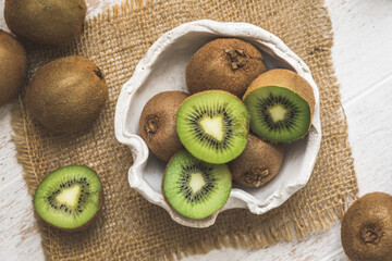 Whole and halfed kiwis in a bowl and on a white wooden table