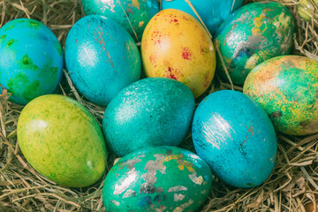 Colorful Easter eggs in blue-green colors with a metallic effect on straw