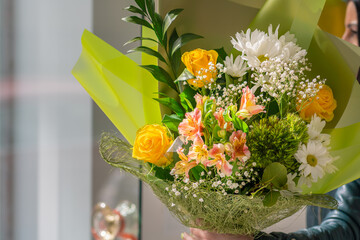 Close-up of a beautiful bouquet of different flowers in a bright light green package in the hand of a woman. Gift, flower salon