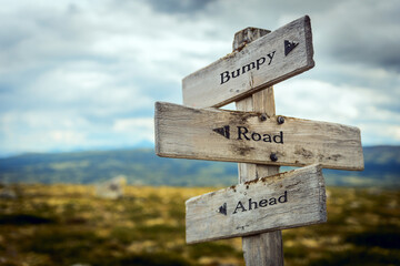 bumpy road ahead text quote written in wooden signpost outdoors in nature. Moody theme feeling.