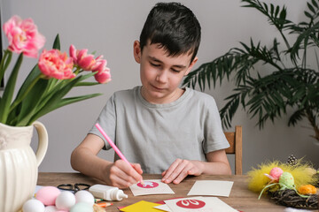 Happy boy making Easter greeting card. Materials for art creativity on kid table, children painting. Paper crafts activity in kindergarten or learning at home