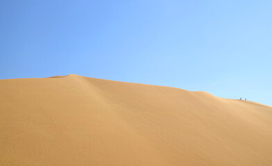 Fototapeta na wymiar Massive sand dune of Huacachina desert with people walking on the top, Ica region of Peru, South America