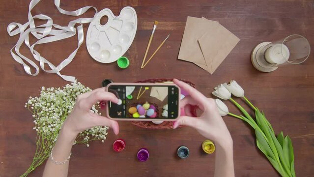 Top view of a table with items to create a composition for Easter. Female hands are photographing a composition on a wooden table on a phone. Church holiday-Easter