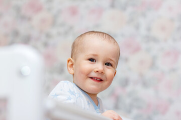 Portrait of cheerful child having fun and laughing spending time in his crib, baby boy dont want to sleep