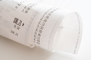 Rolled up shopping receipt, with some amounts visible, on a white surface. Inflation, rising prices and expenses.
