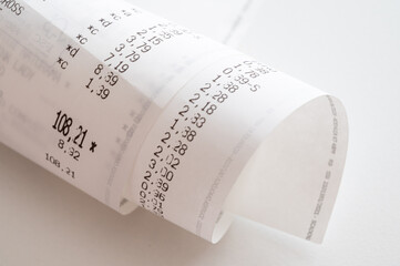 Rolled up shopping receipt, with some amounts visible, on a white surface. Inflation, rising prices...