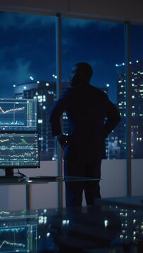 Vertical Portrait of Businessman Looking Out of Window on Late Evening. Modern Hedge Fund Investor Enjoying Successful Life. Urban View with Down Town Street with Skyscrapers at Night with Neon Lights