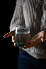 A woman in a gray sweater holds a glass of clean drinking water in her palms. 