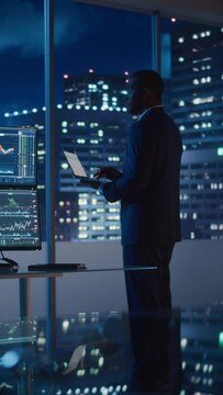 Vertical Footage of Financial Analyst Using Laptop Computer, Standing Next to Multi-Monitor Workstation with Real-Time Stocks Charts. Businesswoman Working in Investment Bank City Office.