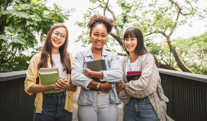 Three young college student happiness holding books talking in the garden.