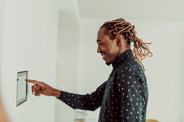 Smiling African American man using modern smart home system, controller on wall, positive young man...