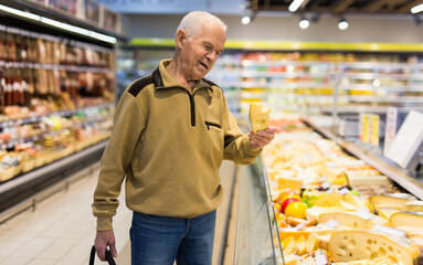 elderly man choosing cheese in supermarket