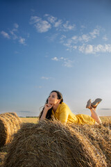 Naklejka na ściany i meble Girl in yellow dress laying and dreaming on a haystack on a field.