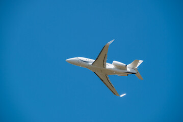 Fototapeta na wymiar White Jet Airplane Taking Off Overhead Blue Sky