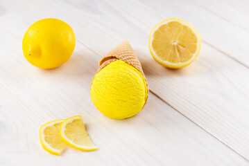 Yellow ice cream in a cone with lemons on a wooden table.
