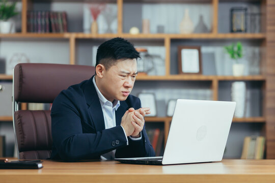 Frustrated and angry asian businessman working on laptop in office, boss shouting at laptop screen