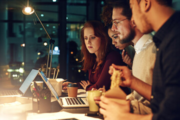 Deadlines wait for no one. Shot of a business team using a laptop together on a night shift at work.