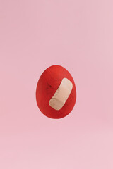 Red cracked Easter egg with band aid over it against pink pastel background. Minimal aesthetic with negative space. Holiday visual.
