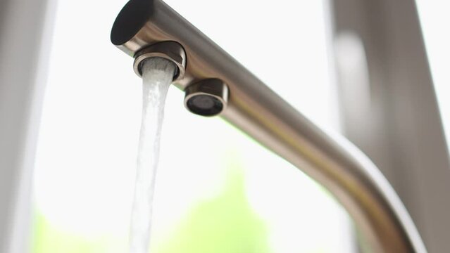 running water flowing from stainless faucet tap with two holes for drinking clean water in kitchen. green natural background, falling splashing stream ow water. economy concept home budget efficiency