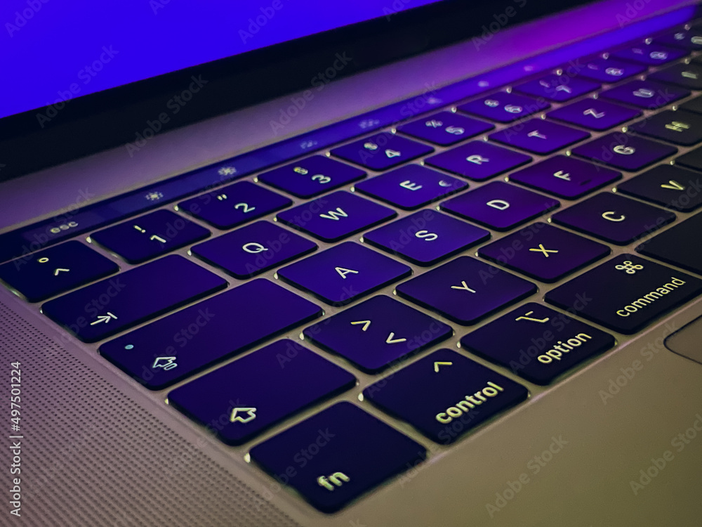Poster closeup of a keyboard of a notebook with violet lighting mirrored from the aluminum frame