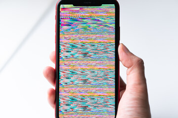 A hand holding smartphone, mobile phone closeup. Glitches, distorted, corrupted image with colorful...