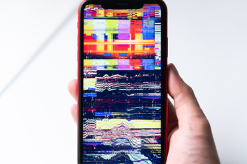 A hand holding smartphone, mobile phone closeup. Glitches, distorted, corrupted image with colorful...